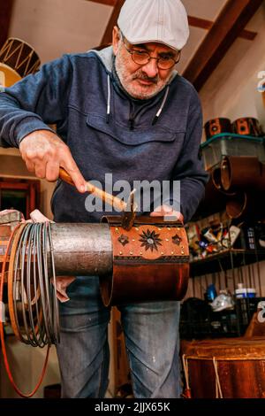Professional male master using hammer while making shell of drum with creative patterns while working in light workshop with special instruments Stock Photo