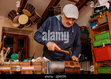 Professional male master using hammer while making shell of drum with creative patterns while working in light workshop with special instruments Stock Photo