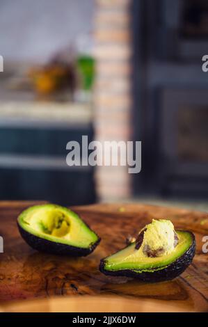 Soft focus of halves of fresh avocado with seed placed on lumber slab during healthy food preparation in kitchen at home Stock Photo
