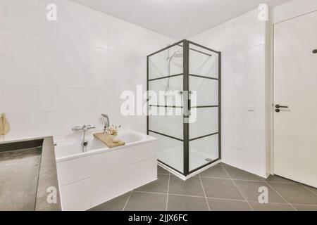 Sinks with mirrors and clean bathtub located near shower box with glass door in modern bathroom with white tiled walls Stock Photo