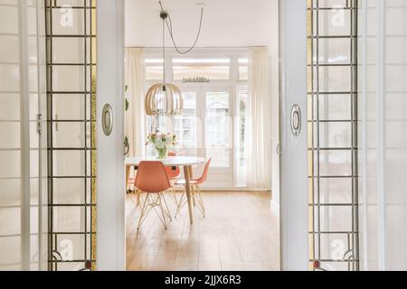 Table and chairs in modern dining room decorated with flowers and lamp placed near door leading to living room Stock Photo