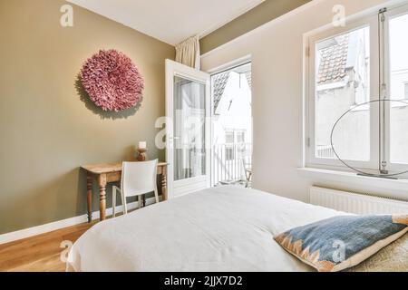 Comfortable bed with soft cushions and blanket placed in contemporary bedroom with work space Stock Photo