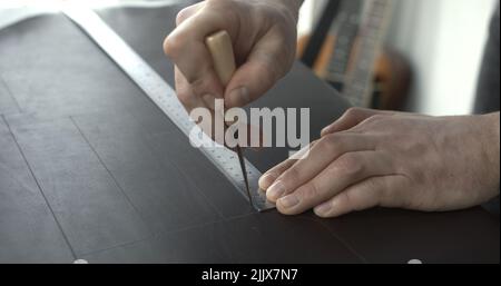 Close up of leather craftsman working with natural leather by awl and ruler. Handmade master at work in local workshop. Leather wallet stitch. Stock Photo
