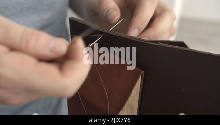 Working process of stitching a brown leather wallet by needle in the leather workshop. Stock Photo