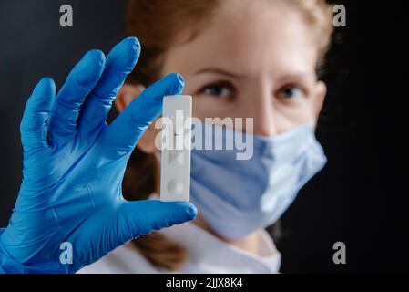 A female doctor or nurse is holding a covid test 19. Physician with test in hand and blue protective medical gloves on black background. Stock Photo