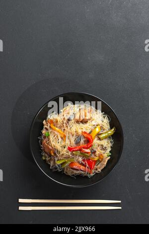 A vertical top view of Korean noodles in a black bowl on a gray table ...