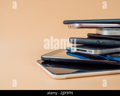 Old smartphones lie on top of each other. Stack of old mobile phones. Smartphones on an orange background. Stock Photo