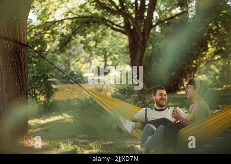 Beautiful couple laughing while relaxing on the hammock in the park Stock Photo