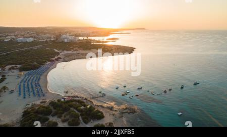 Aerial bird's eye view of Landa beach, Ayia Napa, Famagusta, Cyprus. The landmark tourist attraction golden sand bay at sunrise with sunbeds, sea rest Stock Photo