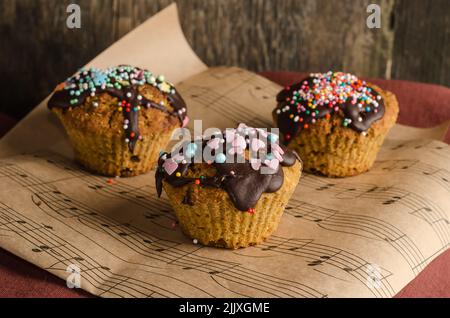 Biscuit cupcakes on paper sprinkled with chocolate with colored sprinkles on a wooden background with selective focus Stock Photo