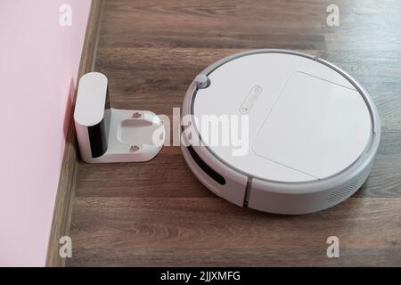 Robotic vacuum cleaner on laminate wood floor charging from base station. Smart cleaning technology. robot vacuum cleaner return to charging at dock Stock Photo