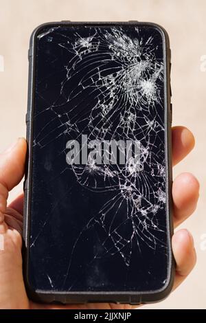 a mans hand holding a smartphone with a shattered screen Stock Photo