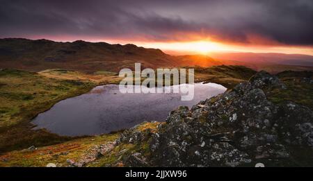 An atmospheric sunrise at the unfrequented Stickle Tarn in Dunnerdale, Lake District. Stock Photo