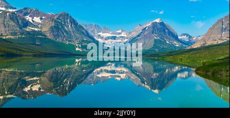Mountain peaks are reflected in the waters of Lake Sherburne, which is located in the Many Glacier region of Glacier National Park, Montana. Stock Photo