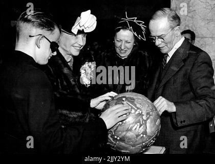 Miss Helen Keller (centre), blind and deaf American authoress 'seeing' the route of her world tour on a braille globe during her visit to braille display in the Courier-Mail vestibule yesterday. With her are Mr. Alan Hinton (left), blind demonstrator at the exhibition, and Miss Polly Thompson, her aide and companion. Visiting Australia in 1948 with Miss Thomson (centre) she was shown a braillie globe of the world by blind demonstrator Alan Hinton at a display in Brisbane. July 28, 1954. Stock Photo