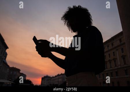 Silhouette of a guy with afro using his smartphone during sunset in the city center Stock Photo