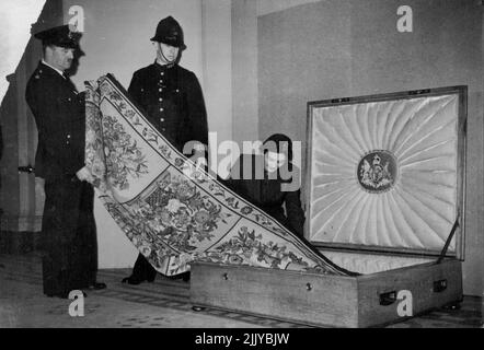 Queen Mary's Carpet For U.S.A. And Canada. -- The carpet being packed in the casket - under police guard - by Miss Patricia Hardie, who will be in charge of it during the journey. The beautiful carpet made by H.M. Queen Mary and presented by her to the nation to help the dollar drive, is being sent to the U.S.A. and Canada, where it will be placed on exhibition to the public. A special Oak and steel casket has been constructed to preserve the carpet from damage during its travels. March 15, 1950. (Photo by Sports & General Press Agency Limited). Stock Photo