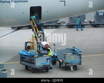 Luggage baggage handlers unloading a KLM aeroplane at Schiphol Airport, Amsterdam, the Netherlands