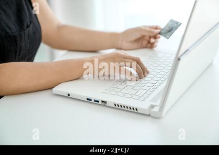 Young woman makes online purchases sitting in front of laptop with bank card in her hand. Hands close-up. Concept of online shopping and money transfer. Stock Photo