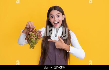 amazed child holding fresh grapes fruit on yellow background Stock Photo