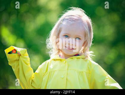 Sweet little blond girl toddler in yellow raincoat. Stock Photo