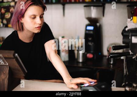 Young female barista working at checkout counter in coffee shop Stock Photo