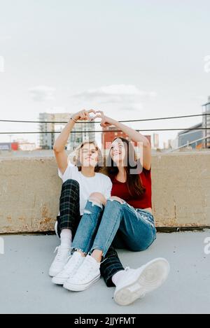 boyfriend and girlfriend sitting on rooftop making heart symbol Stock Photo