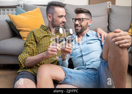 Romantic gay couple smiling and drinking wine at home. High quality photography. Stock Photo
