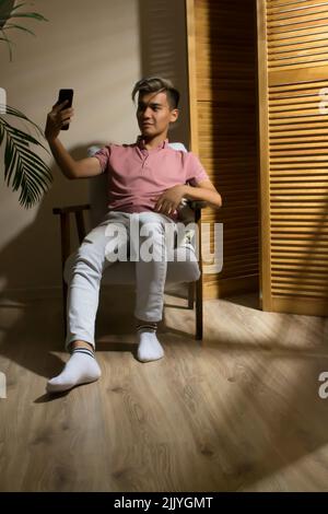 Man sitting in an armchair make selfie using smartphone Stock Photo