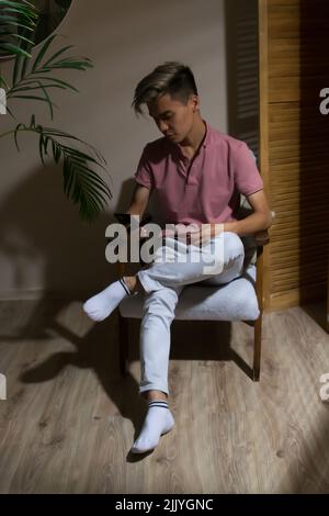 Businessman sitting in an armchair using smartphone at home Stock Photo
