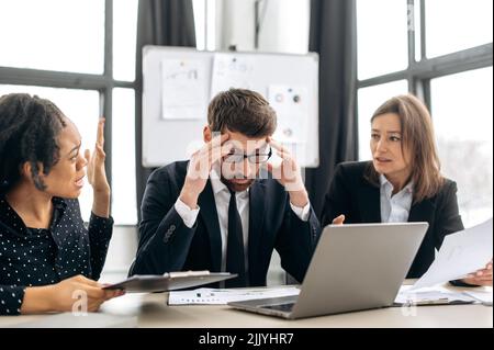 Quarrel in the work team. Irritated business employees of different nationalities, work at the workplace in modern office, argue over work issues, cannot agree, experience stress from working together Stock Photo