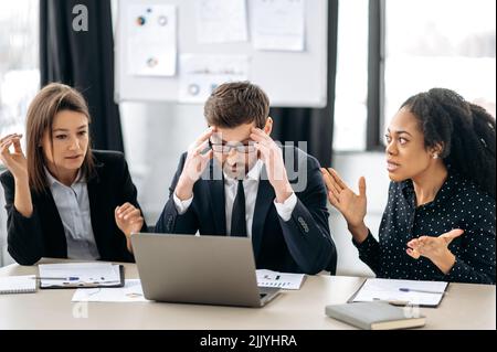 Annoyed business employees of different nationalities, work at the workplace in modern office, argue over work issues, cannot agree, experience stress from working together. Quarrel in the work team Stock Photo
