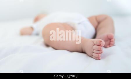 Newborn chubby foots over white background. Close up new born baby body part. Peace calm infant toddler boy laying on soft white blanket. Family mater Stock Photo