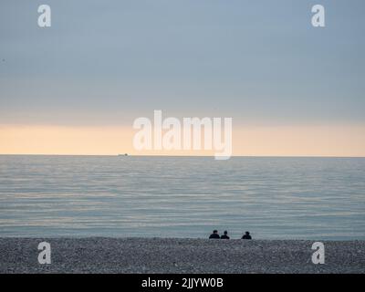 People are sitting on the seashore. Coastline at sunset. Rest on the sea. People silhouettes Stock Photo