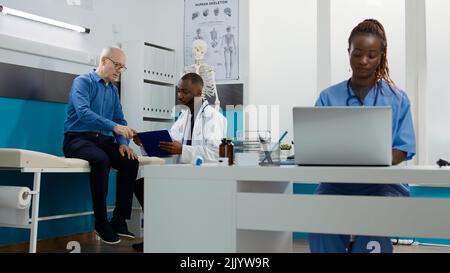 General practitioner consulting old man in facility office, taking notes to give prescription medicine and treatment. Medic doing checkup examination appointment with senior patient at clinic. Stock Photo