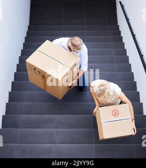 Wherever we go, we get to make new memories. a mature couple carrying boxes up the stairs on moving day. Stock Photo