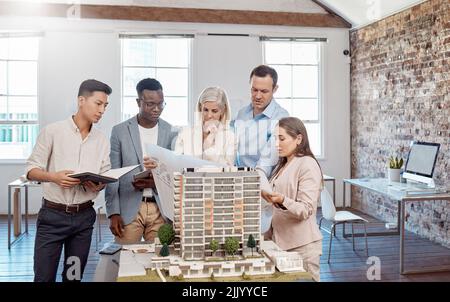 A diverse team of architects working on a building model together inside the office. A group of engineers planning a reconstruction or design project Stock Photo