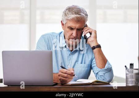 Give me the details... a mature man making notes while talking on his cellphone. Stock Photo