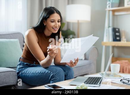 Im on the right track with my savings. an attractive young woman sitting alone in her living room at home and calculating her finances. Stock Photo