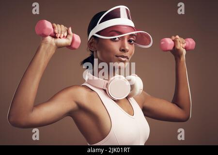 Working out to my own rhythm today. an attractive young woman standing alone in the studio and using dumbbells while working out. Stock Photo