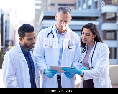 We cant put our heads into pillows. doctors using a digital tablet while outside in the city. Stock Photo