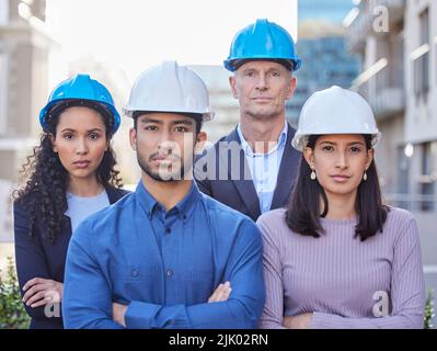 There isnt a challenge we cant overcome. a diverse group of businesspeople standing together with their arms folded while wearing hardhats. Stock Photo