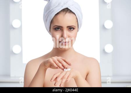 Pretty smiling young woman applying cream on her hands Stock Photo