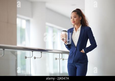 Pensive young Asian business lady drinking coffee Stock Photo