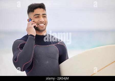 Im catching waves right now. a young man using a cellphone while surfing at the beach. Stock Photo