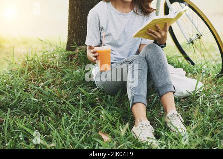 Cropped image of female student drinking cocktail and reading a book in the park Stock Photo