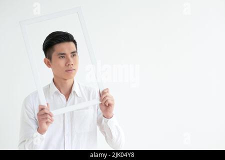 Handsome Vietnamese young man looking through white picture frame Stock Photo