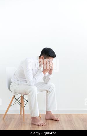 Tired frustrated young man sitting on chair and covering his face with arms Stock Photo