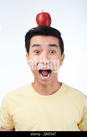 Portrait shot of scared Asian man with red apple on head looking at camera and shouting at top of voice, isolated on white background Stock Photo