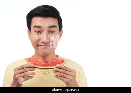 Head and shoulders portrait of smiling Asian man holding slice of juicy watermelon while standing against white background Stock Photo